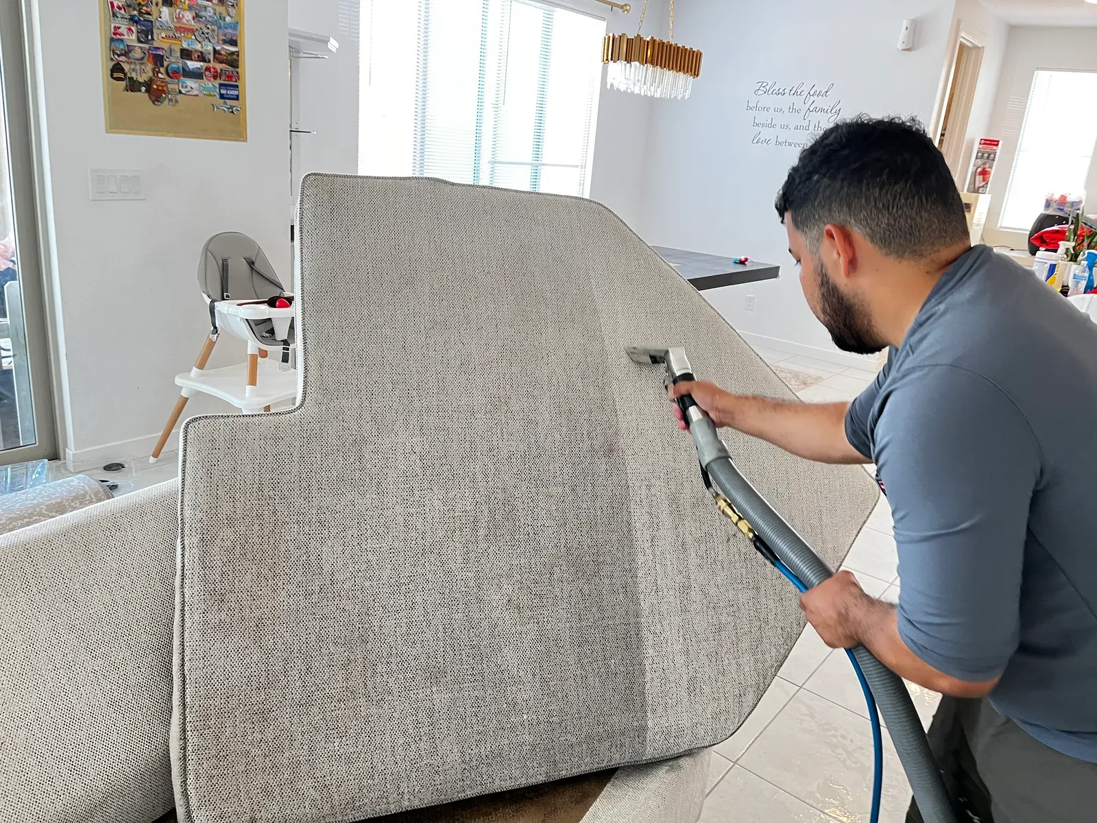 Technician deep cleaning a gray upholstered sofa with a handheld extraction tool in a Las Vegas home