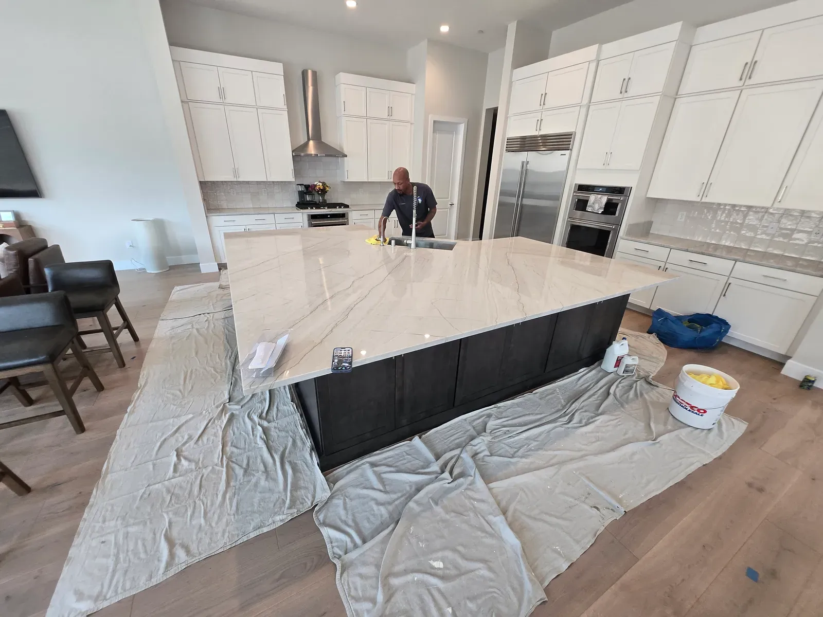 Royal Surface Restore technician sealing a large white quartzite kitchen island with drop cloths down in a Las Vegas home