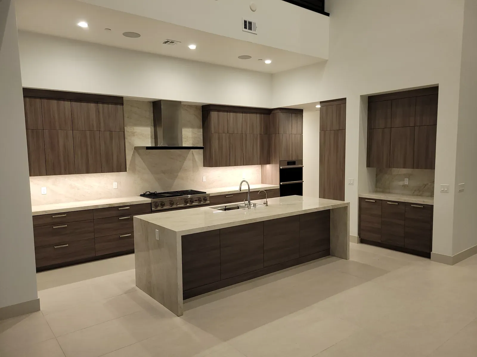 Sealed white quartz waterfall island in a modern Las Vegas kitchen with dark wood cabinets