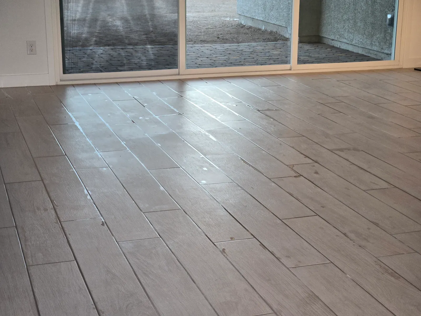 Wood-look plank tile floor with freshly applied grout sealer in an empty Las Vegas room with patio doors