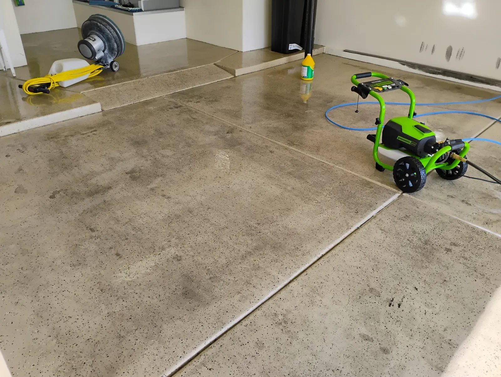 Pressure washer and floor buffer cleaning a residential garage concrete floor in Las Vegas