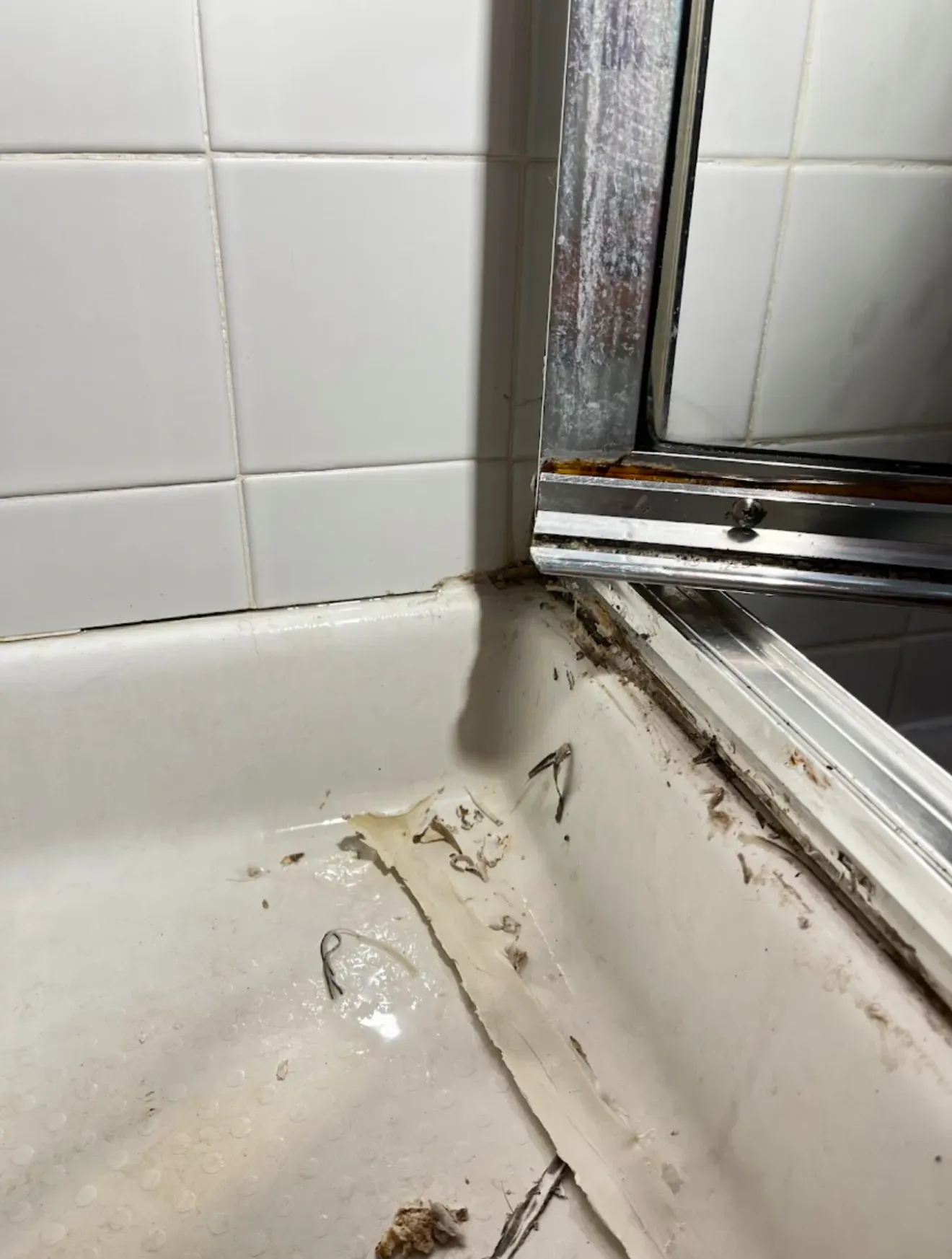Close-up of a grimy shower door track and pan before rejuvenation cleaning in a Las Vegas bathroom
