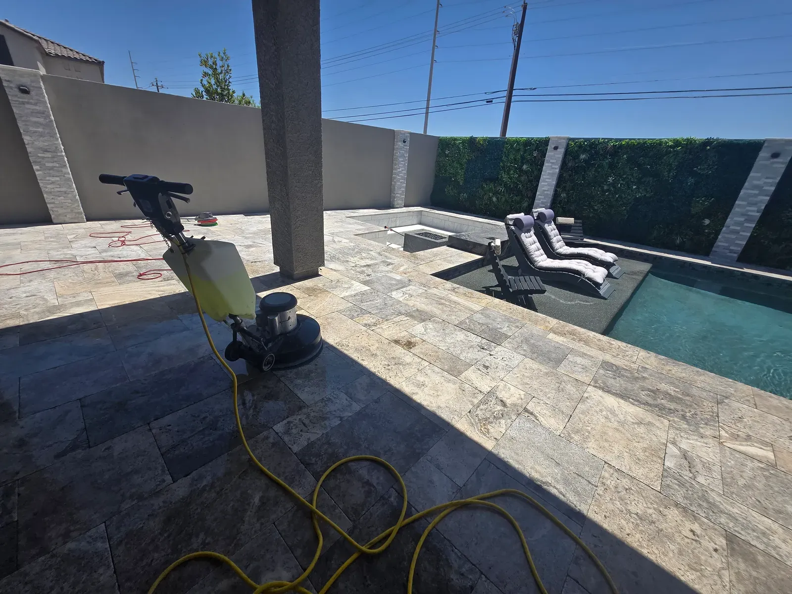 Rotary floor machine cleaning a travertine pool deck beside a pool in a Las Vegas backyard