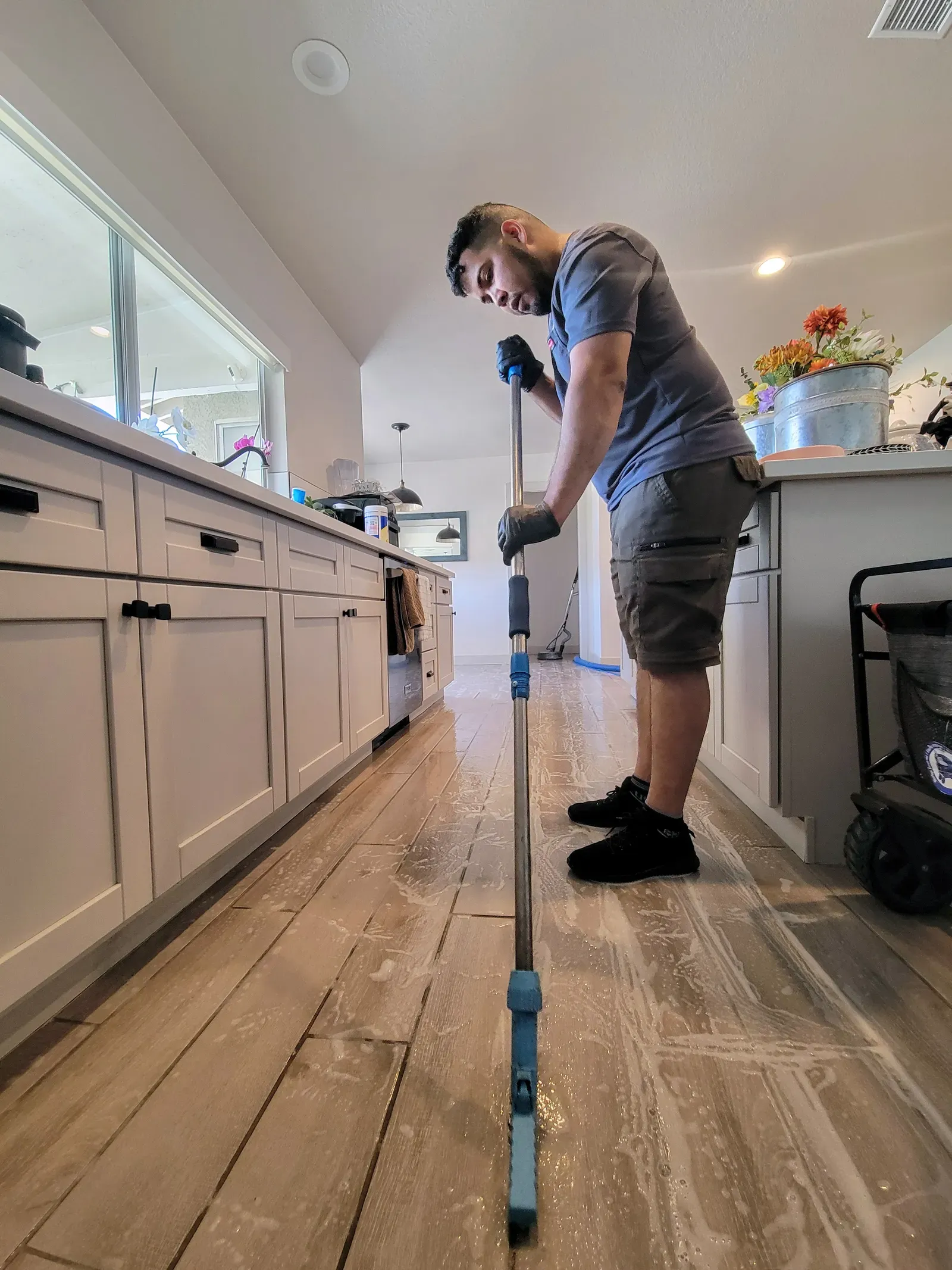 Technician scrubbing soapy cleaner across a wood-look plank tile kitchen floor in a Las Vegas home